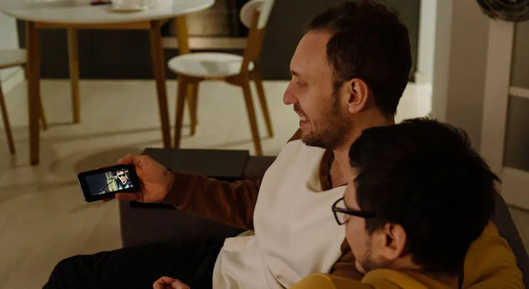Two friends relaxing on a couch, streaming a show together on a smartphone